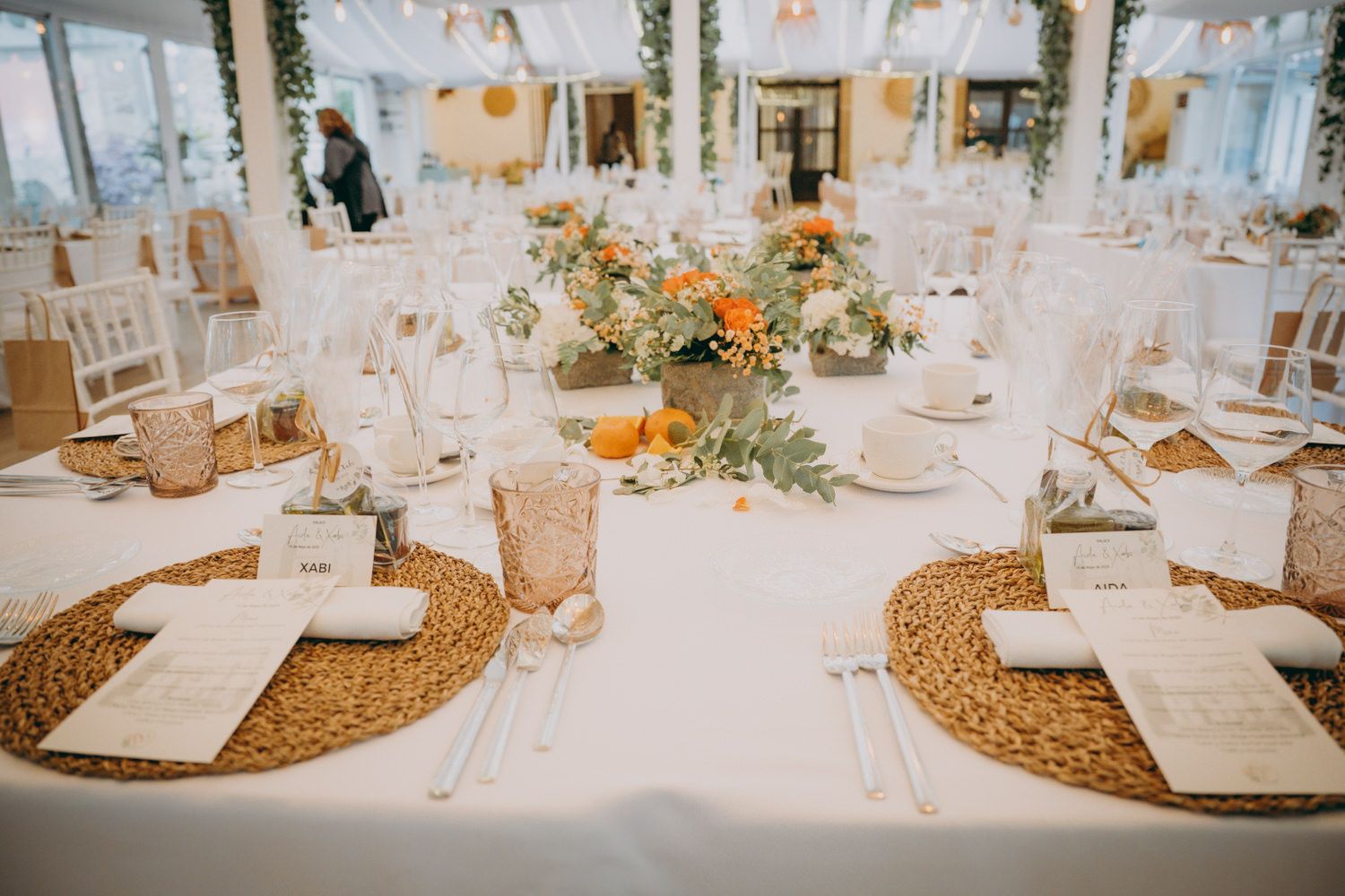Mesa de recepción de boda con manteles individuales tejidos, mantelería blanca y centros de mesa florales.
