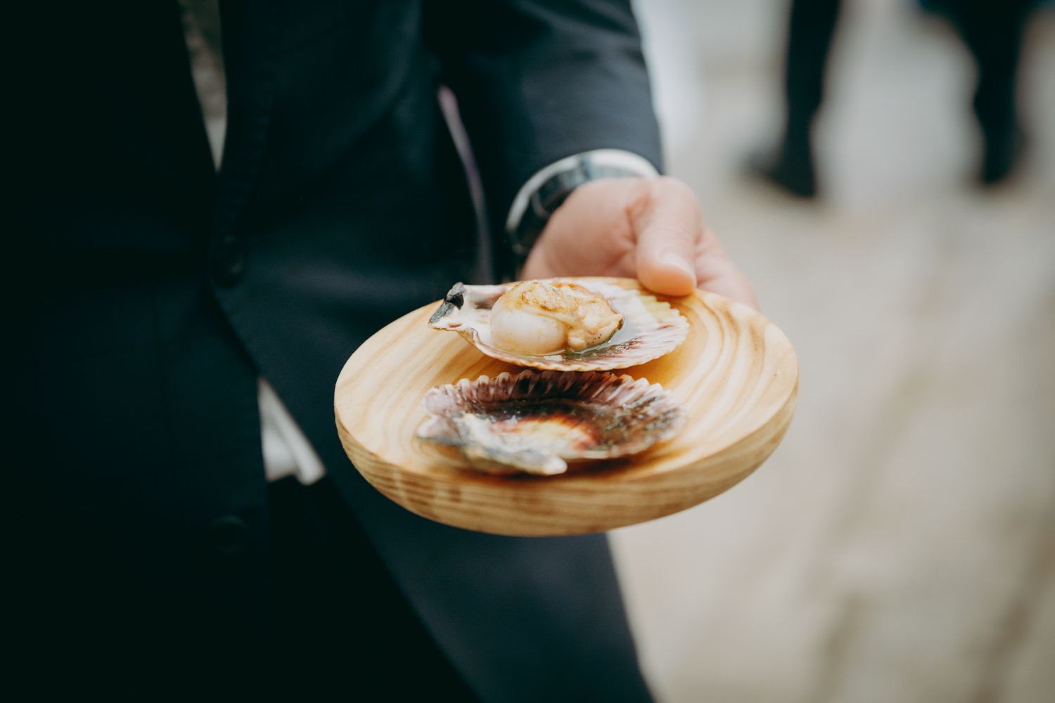 Servidor sosteniendo un plato de madera con ostras frescas y guarnición servida en una boda del Palacio de Villabona.