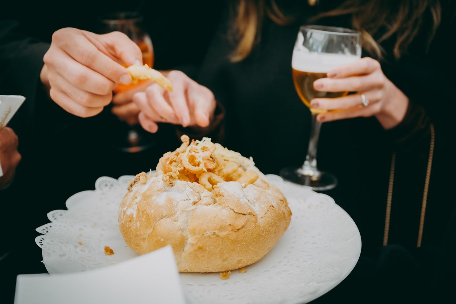 Un panecillo crujiente cubierto con queso rallado y servido con un vaso de cerveza.