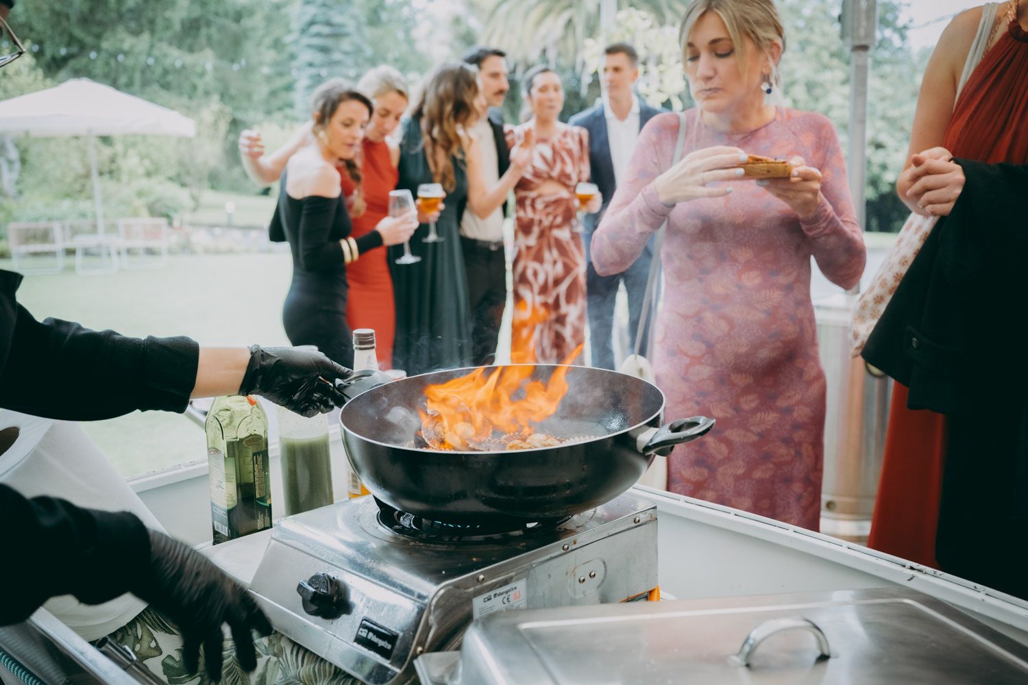 Un chef cocinando con llamas en una sartén en un evento de catering al aire libre.
