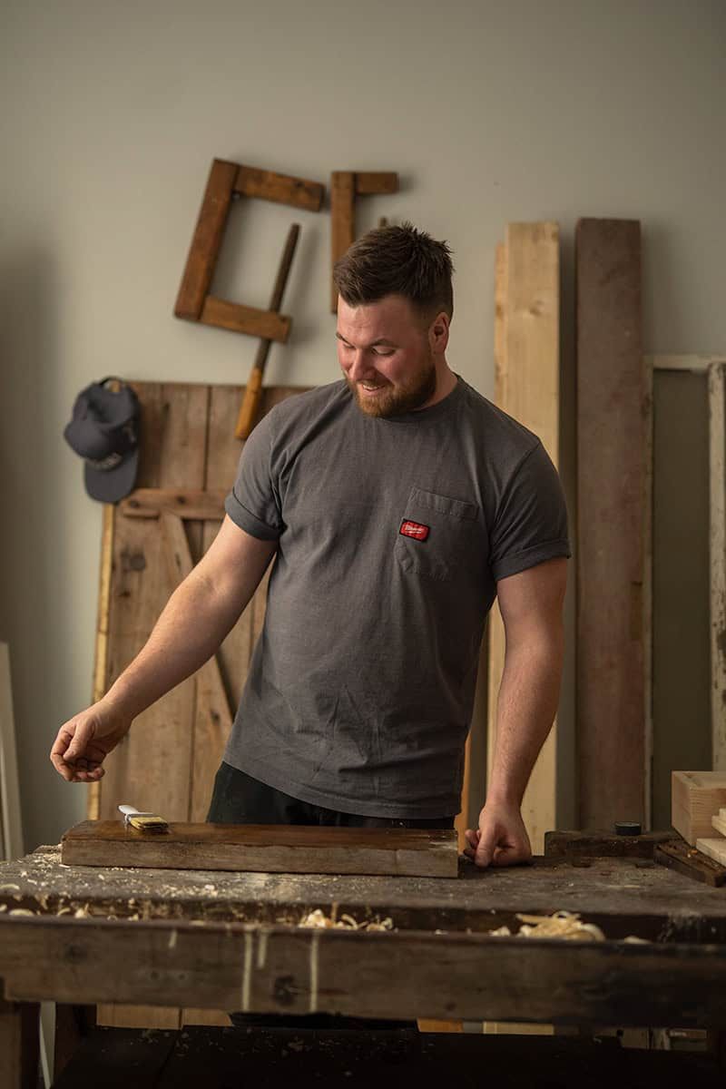 A craftsman working at a wooden workbench in a workshop with tools on the wall.