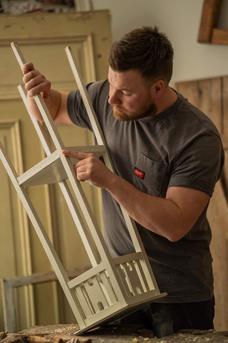 A woodworker examining a white wooden frame structure in a workshop.