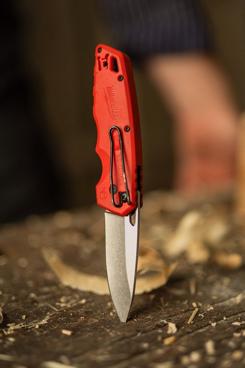 A red pocket knife with silver blade against a dark wooden surface.