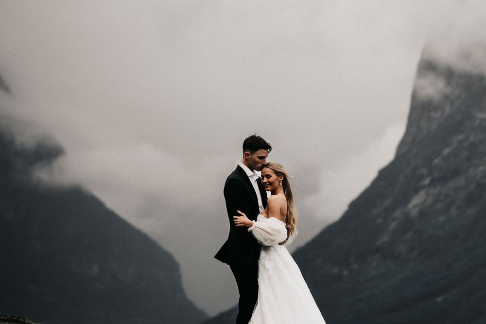 A couple in wedding attire embraces against a dramatic backdrop of misty mountain peaks on their special day.