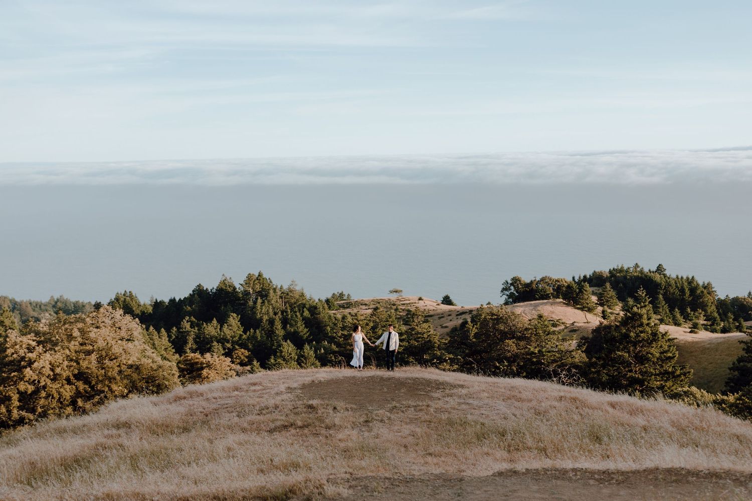 A couple embraces on a sandy beach with dramatic cliffs and crashing waves along the California coastline.