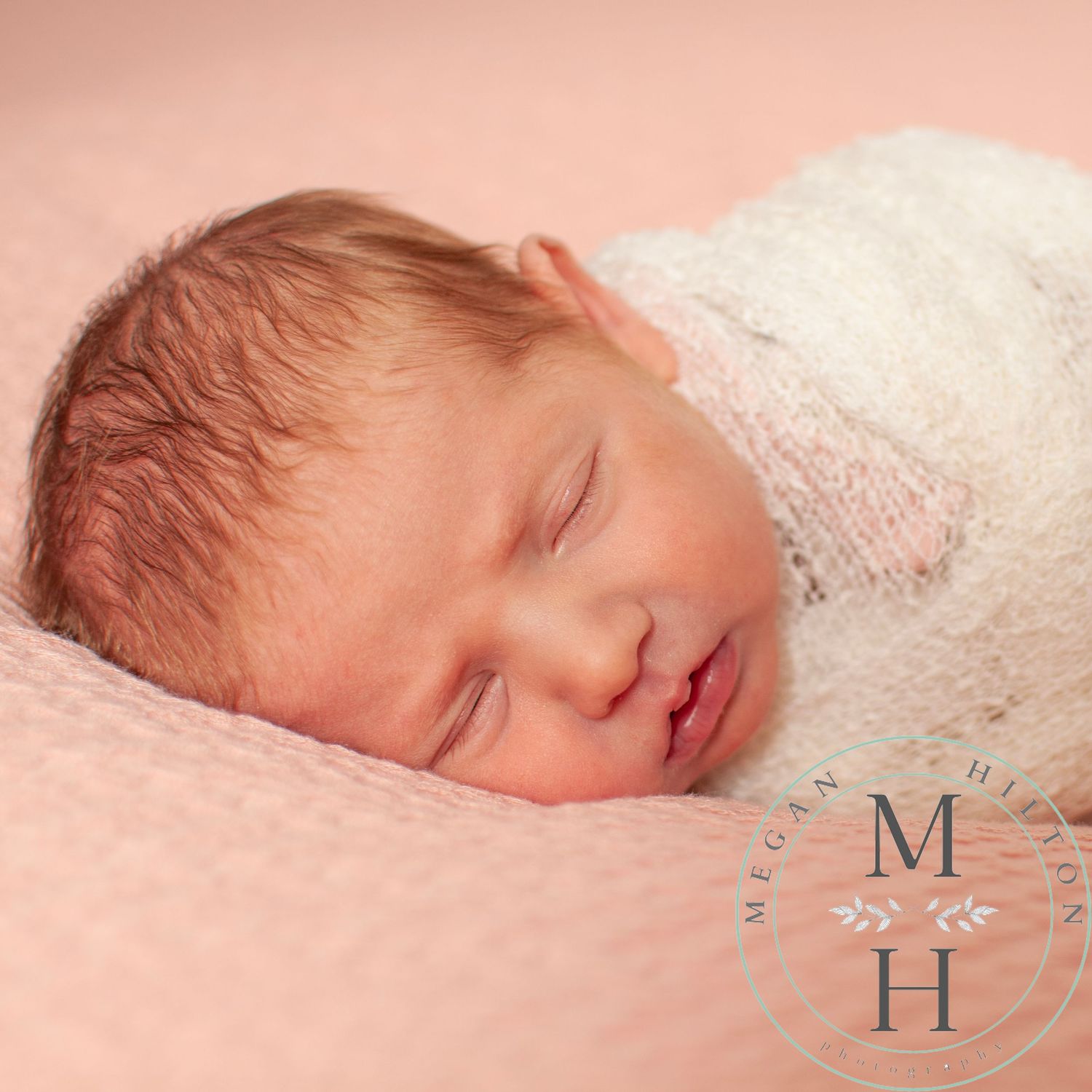 Photograph of a sleeping newborn baby with light hair swaddled in soft white fabric rests against a pink background.