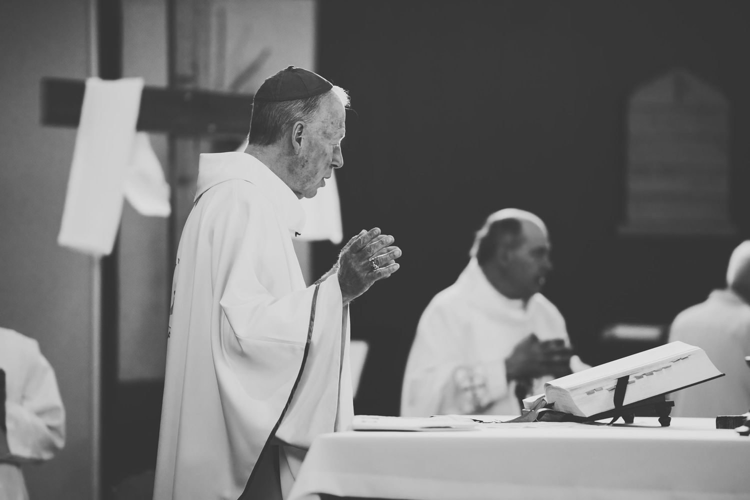 Black and white image shows a bishop performing a catholic mass ceremony at the alter.