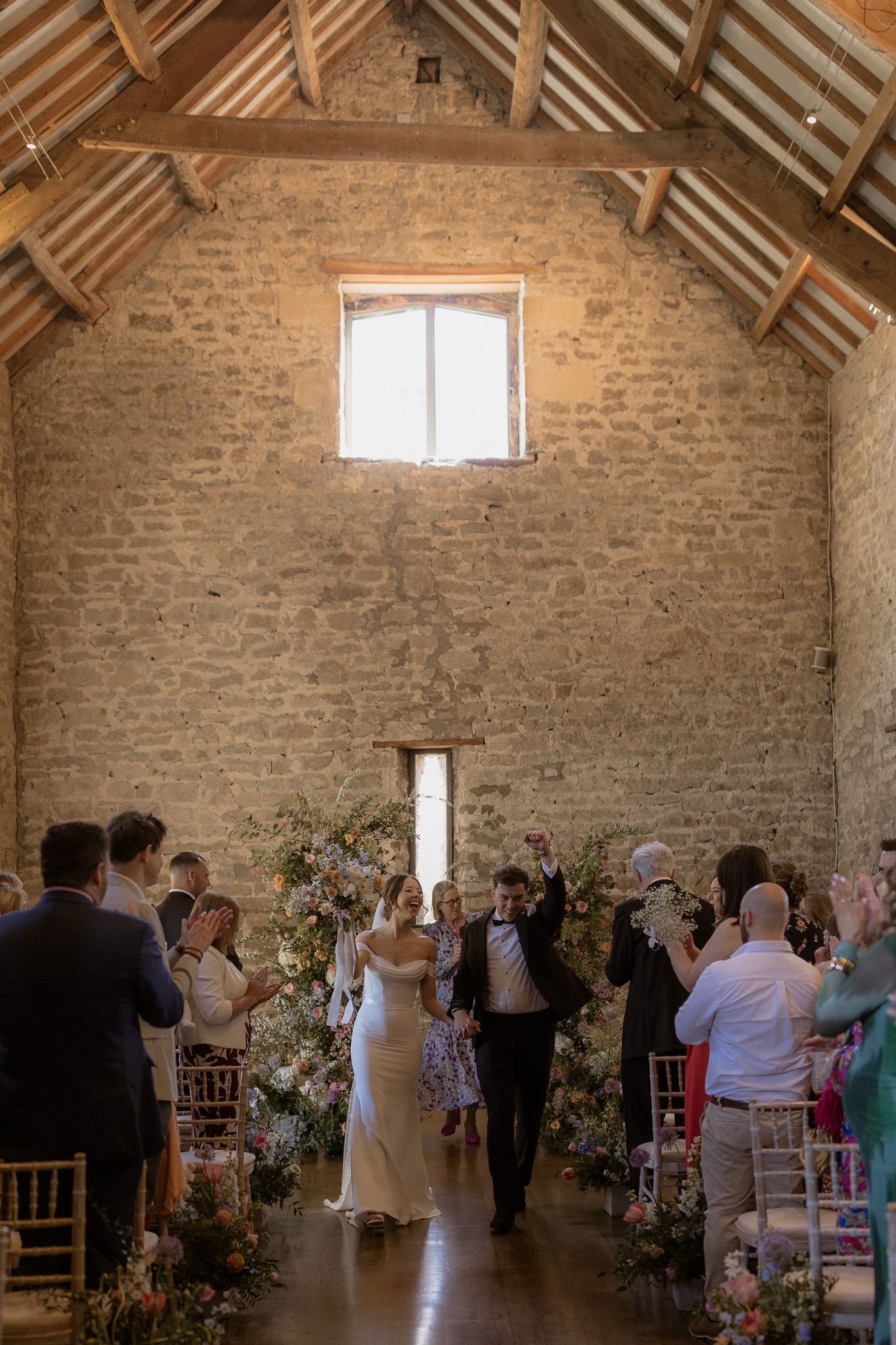 A wedding ceremony in a rustic barn venue with stone walls and wooden beams.