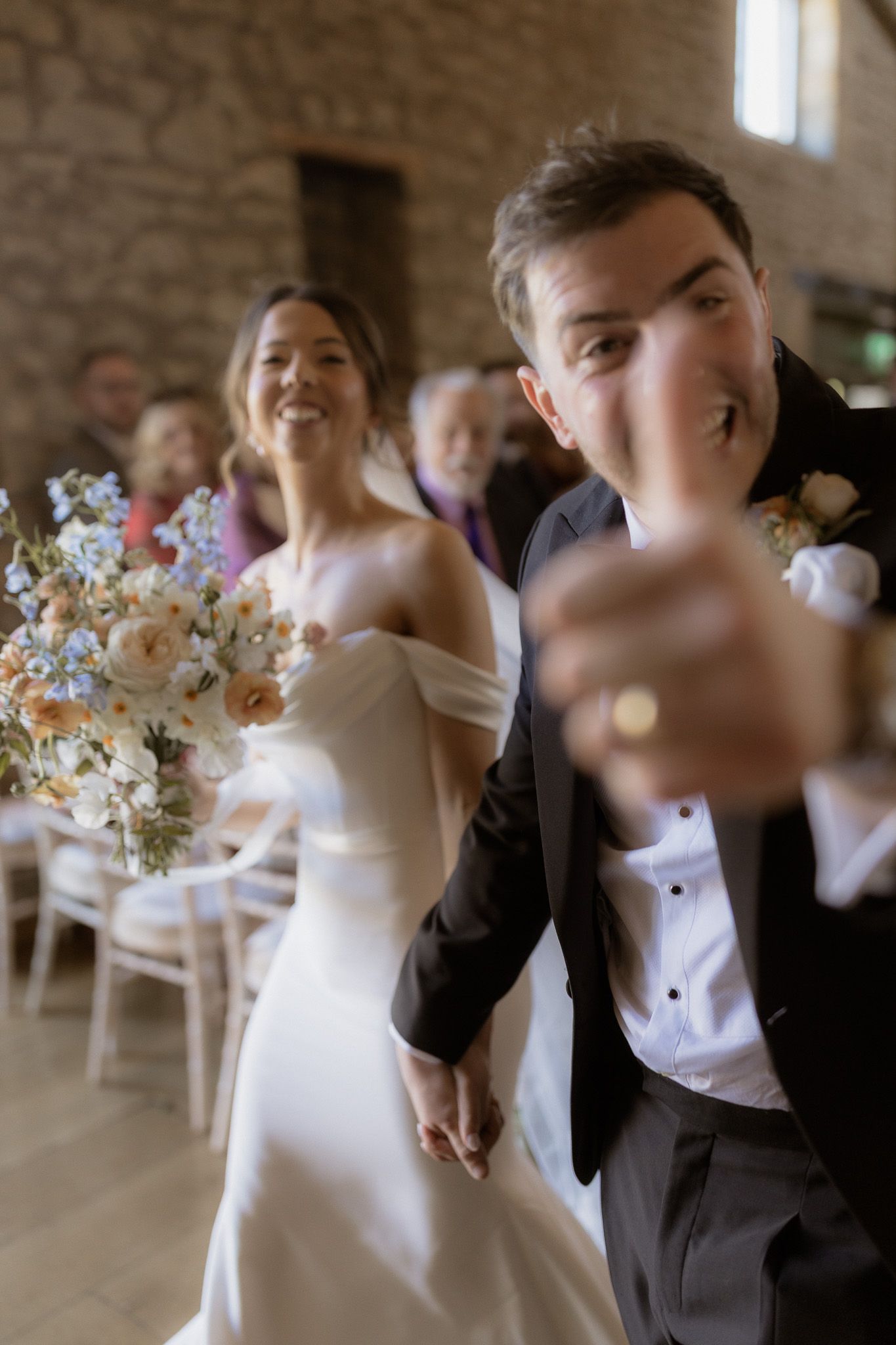 A newlywed couple shares a joyful moment on their wedding day in a rustic brick venue with floral decorations.