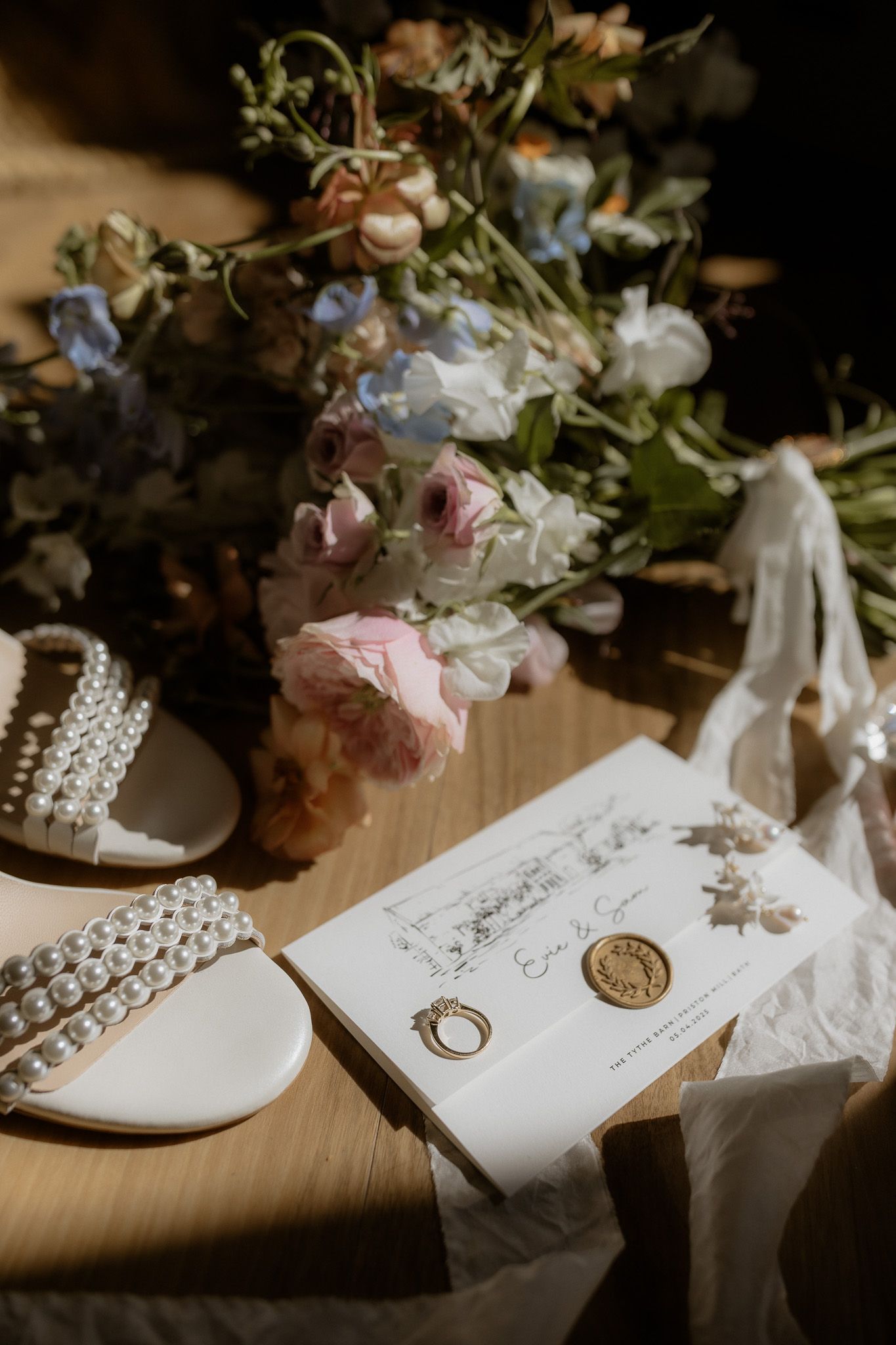 Wedding details including floral arrangements, wedding rings, and delicate lace on a rustic wooden surface in natural light.