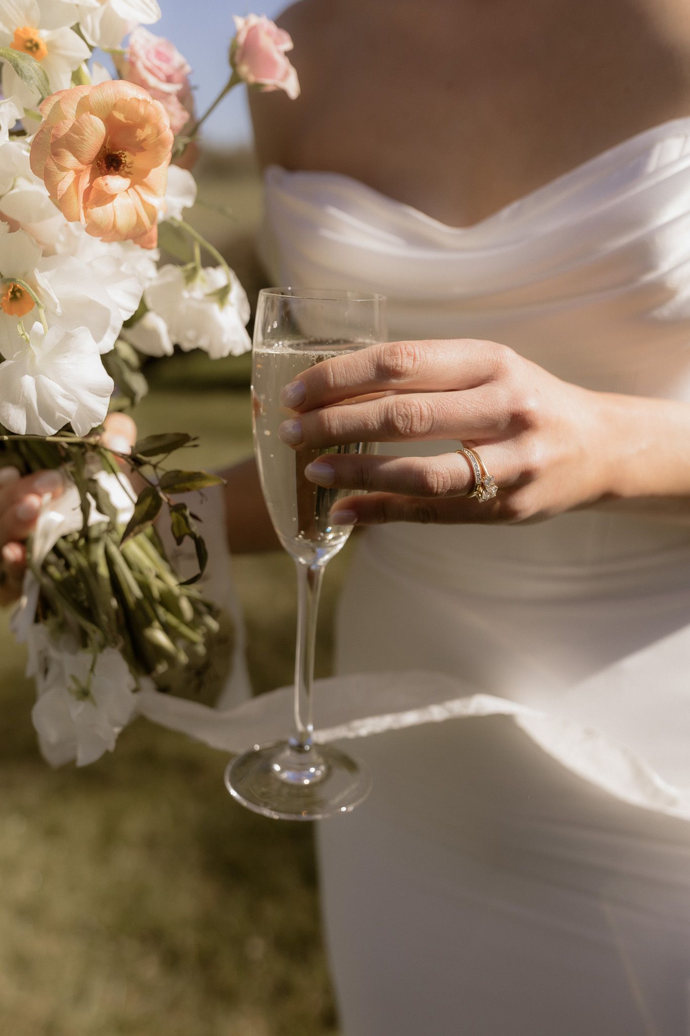 Close up of bride holding champagne glass with delicate peach and white floral bouquet.