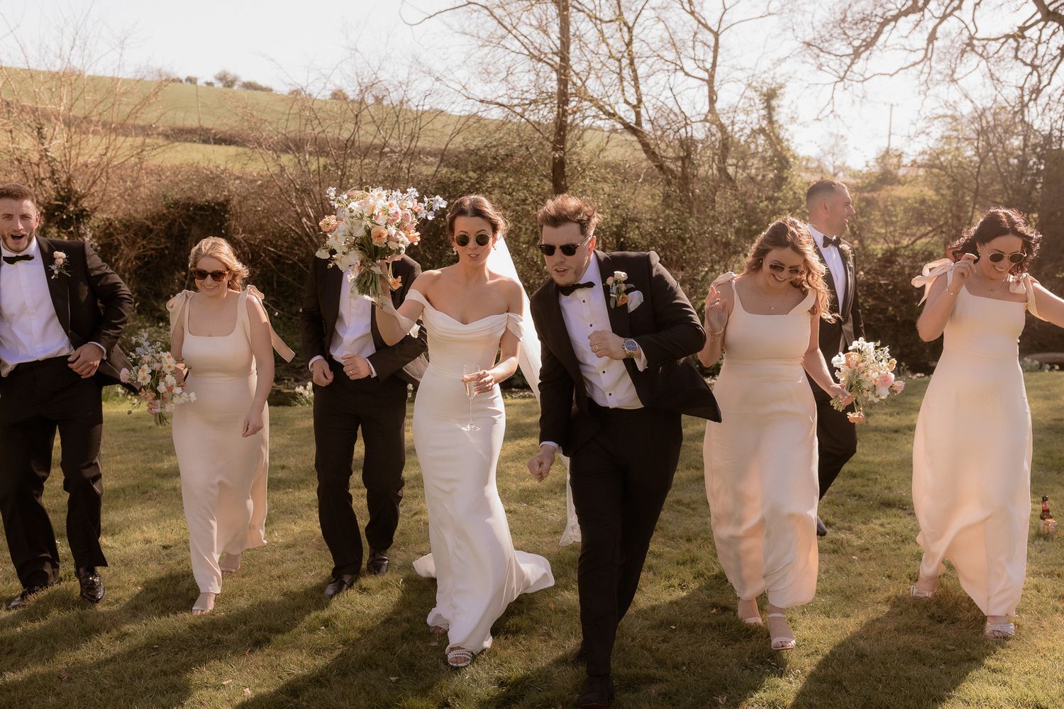 Wedding party walking and laughing together in a sunny field.