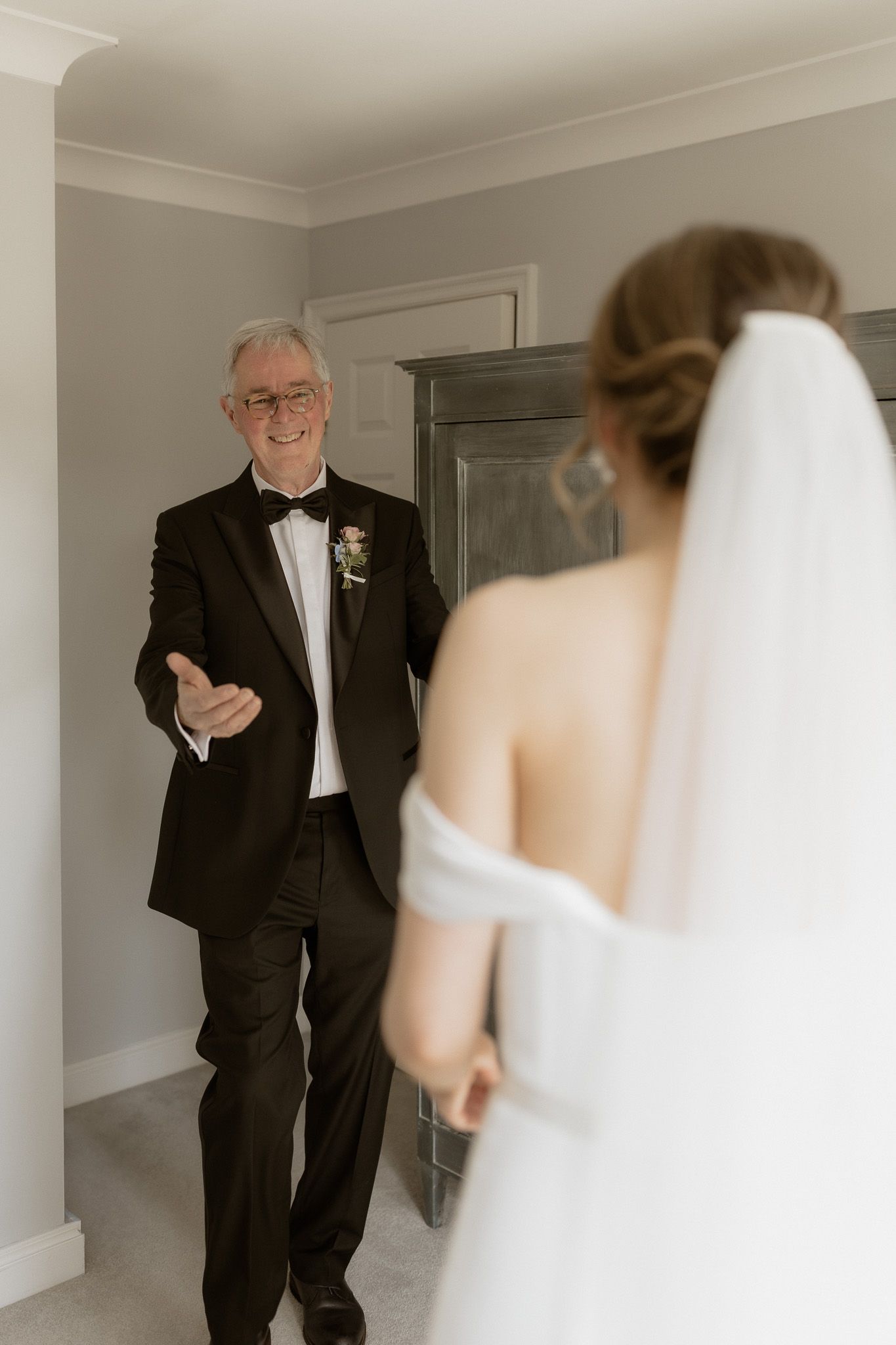 An emotional first look moment between a father in a black tuxedo and his daughter in a white wedding dress.