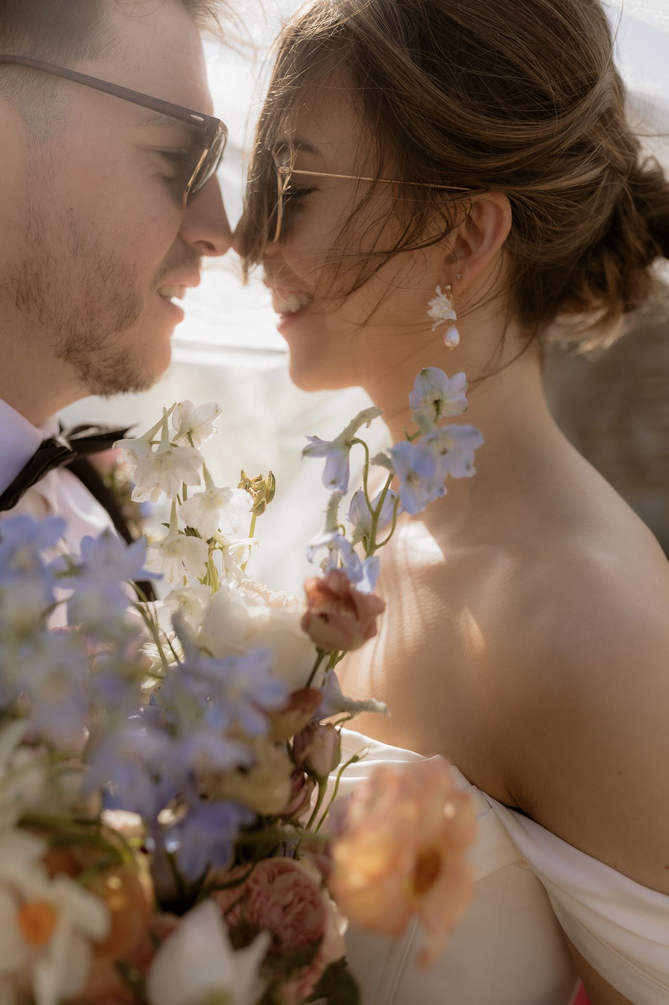 Romantic wedding photo showing couple in close embrace with delicate flowers and soft sunlit glow.