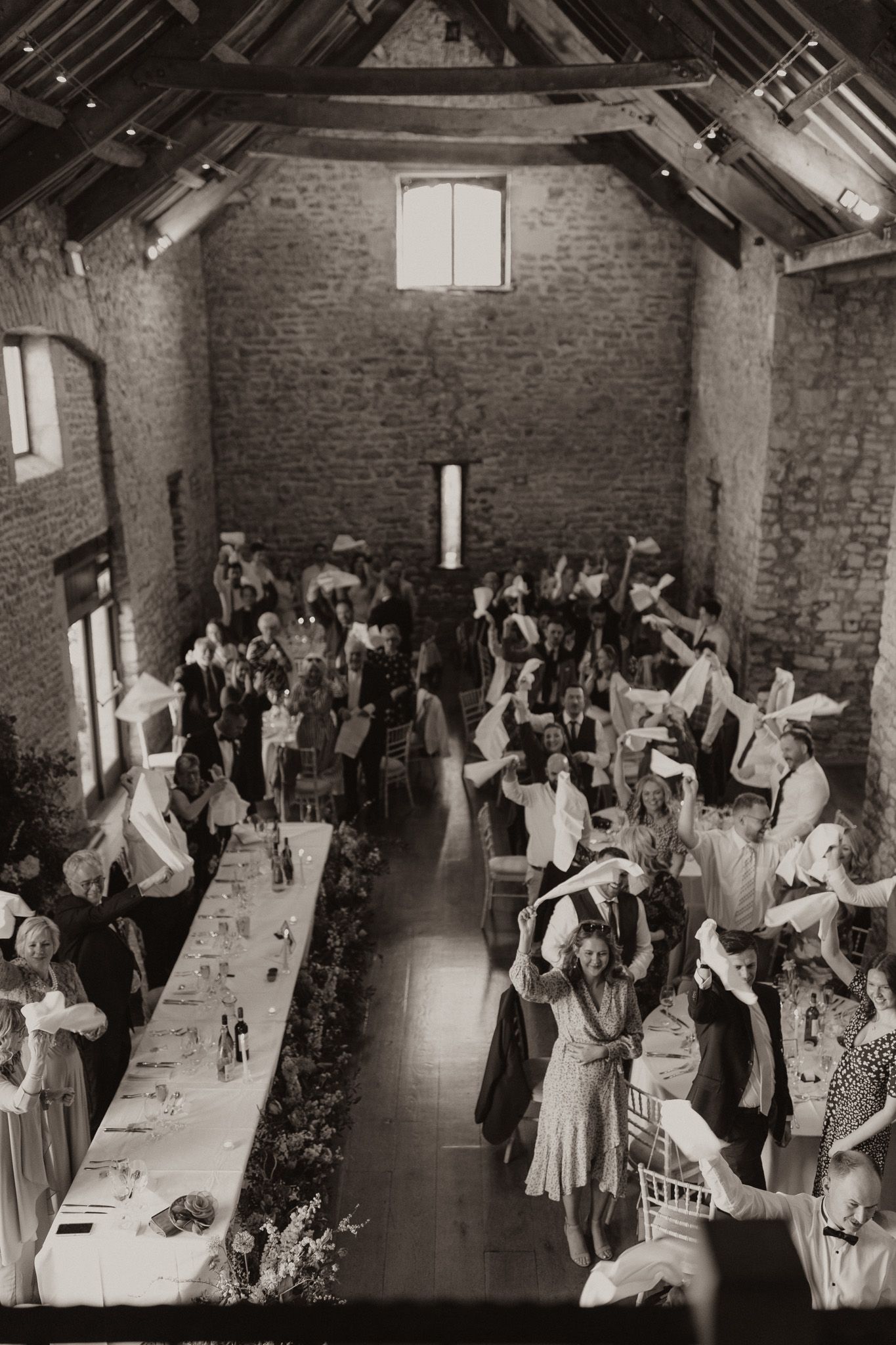 Vintage black and white photo of wedding reception guests dancing in a rustic brick venue.