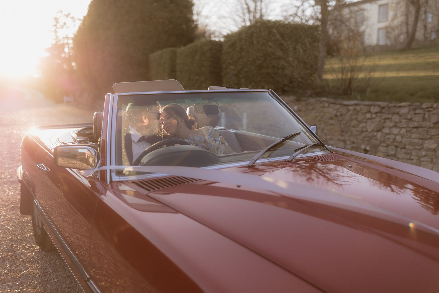 A couple shares a romantic moment in a classic red convertible car at sunset.