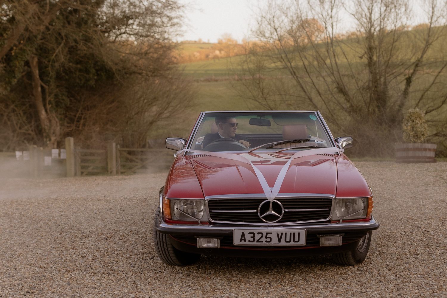 Classic red Mercedes sports car decorated with white wedding ribbons parked on a country driveway.