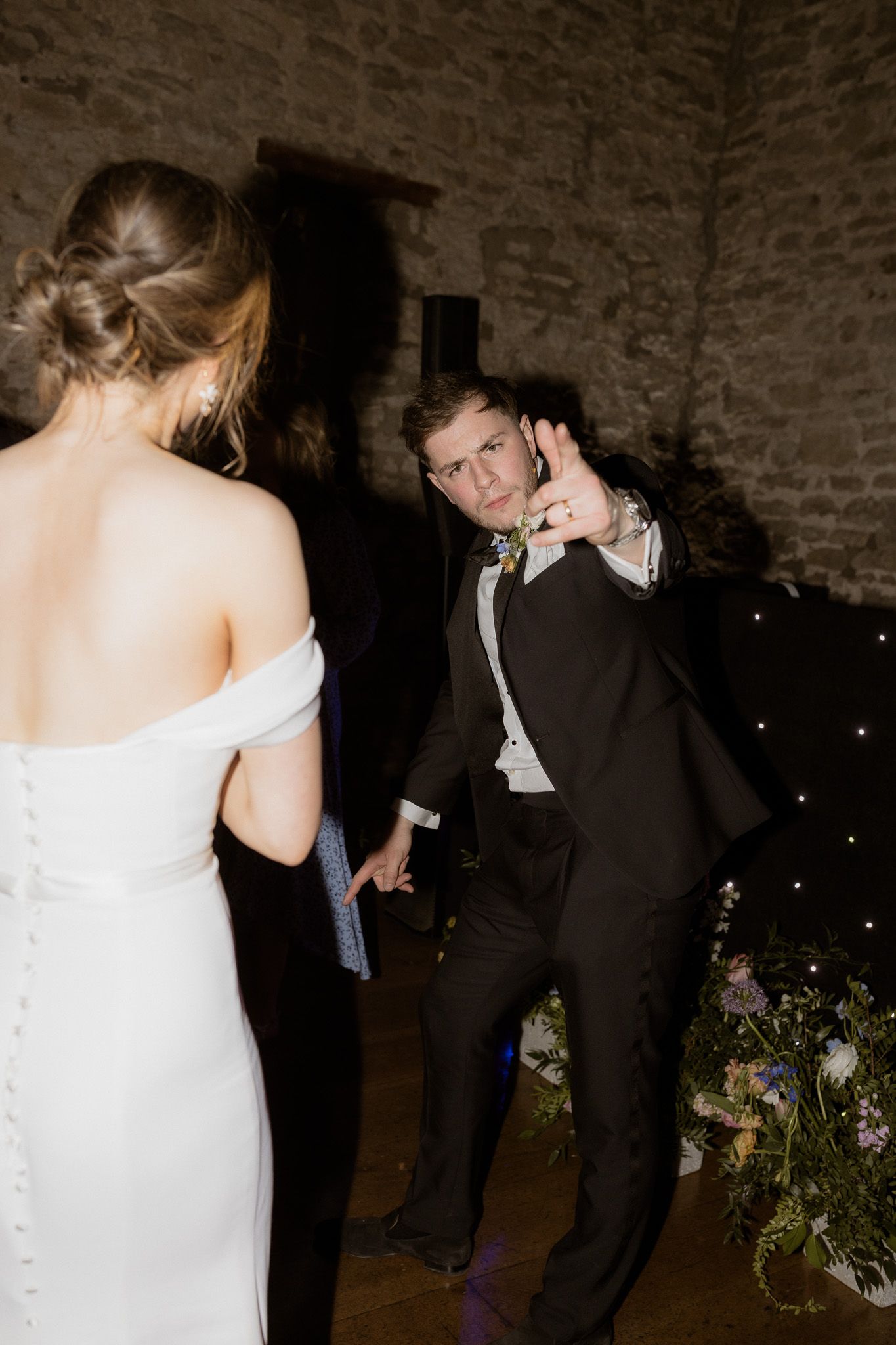 A couple dances together in a rustic stone-walled venue decorated with twinkling lights.