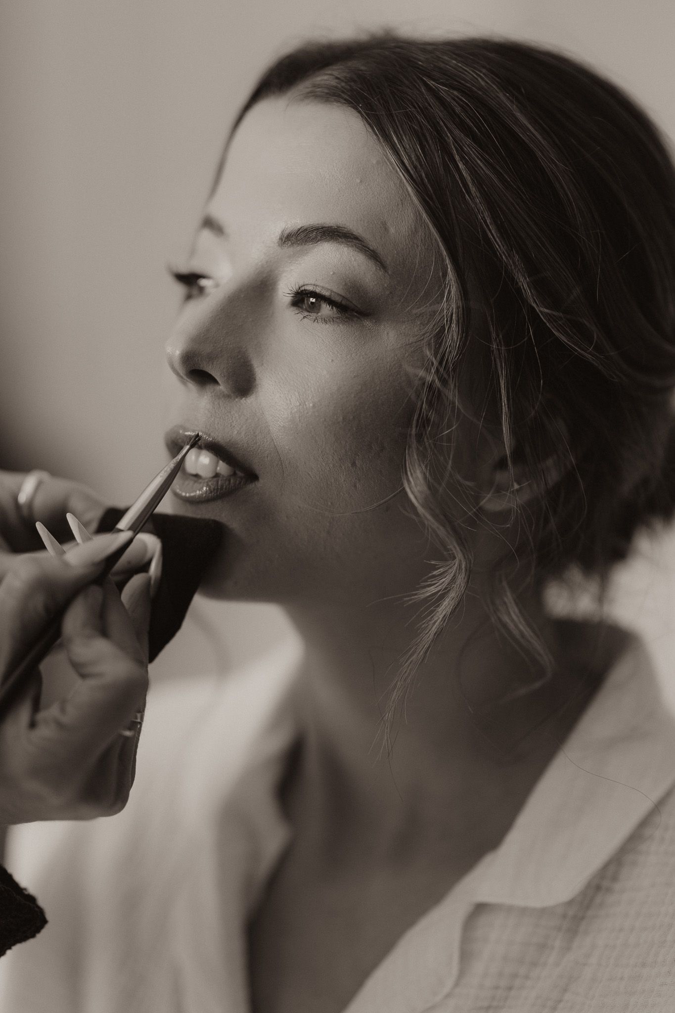 A black and white beauty shot of a woman having lipstick applied during wedding preparations.