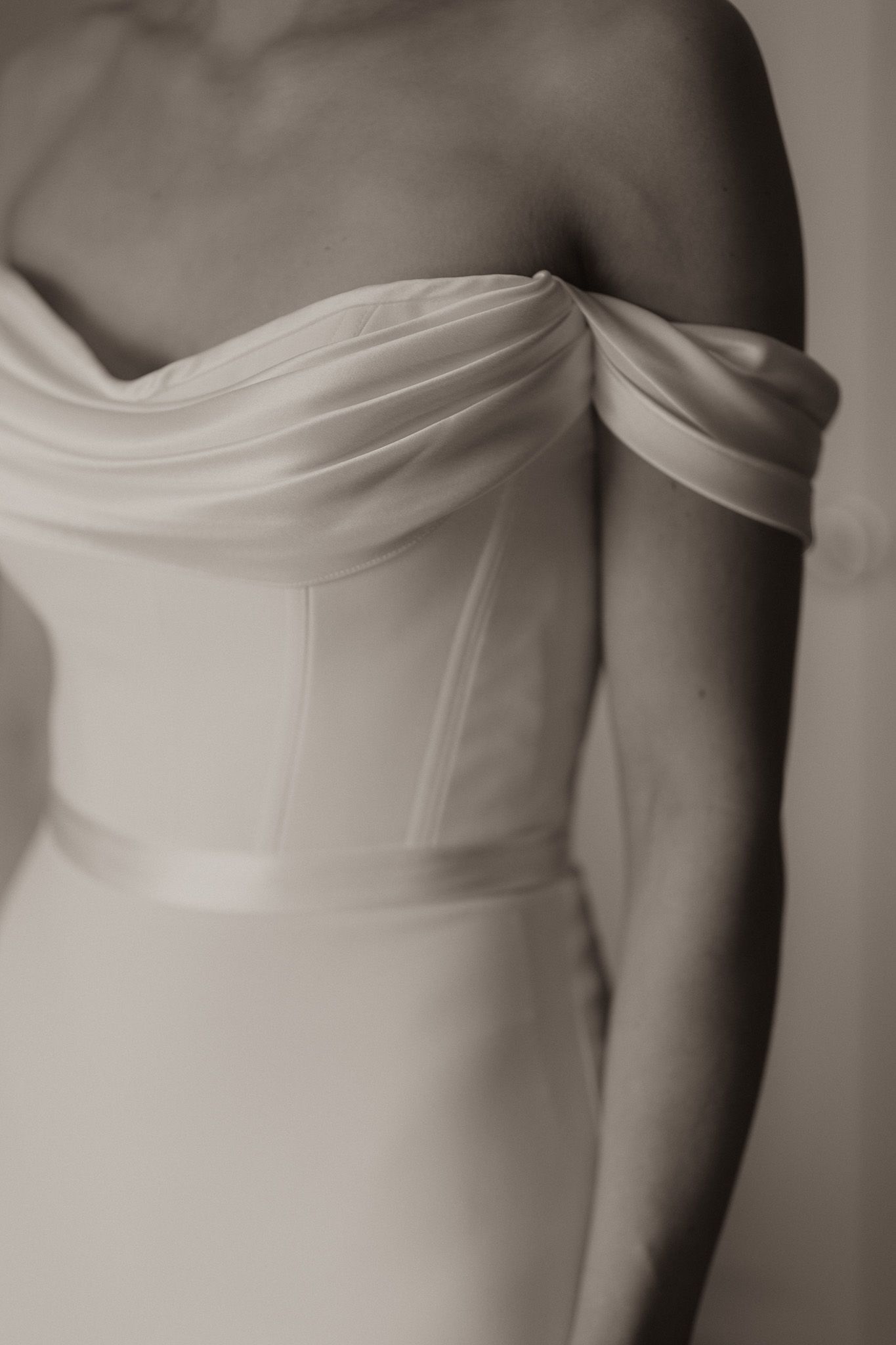 Close-up detail of an elegant off-shoulder white wedding dress showing draped fabric and structured bodice.
