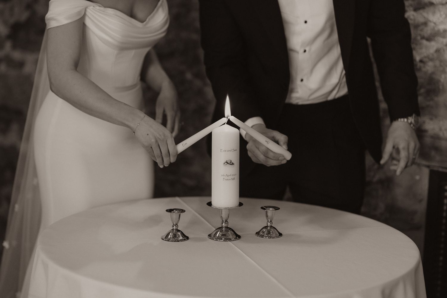 Monochrome closeup of couple lighting unity candle together during wedding ceremony.