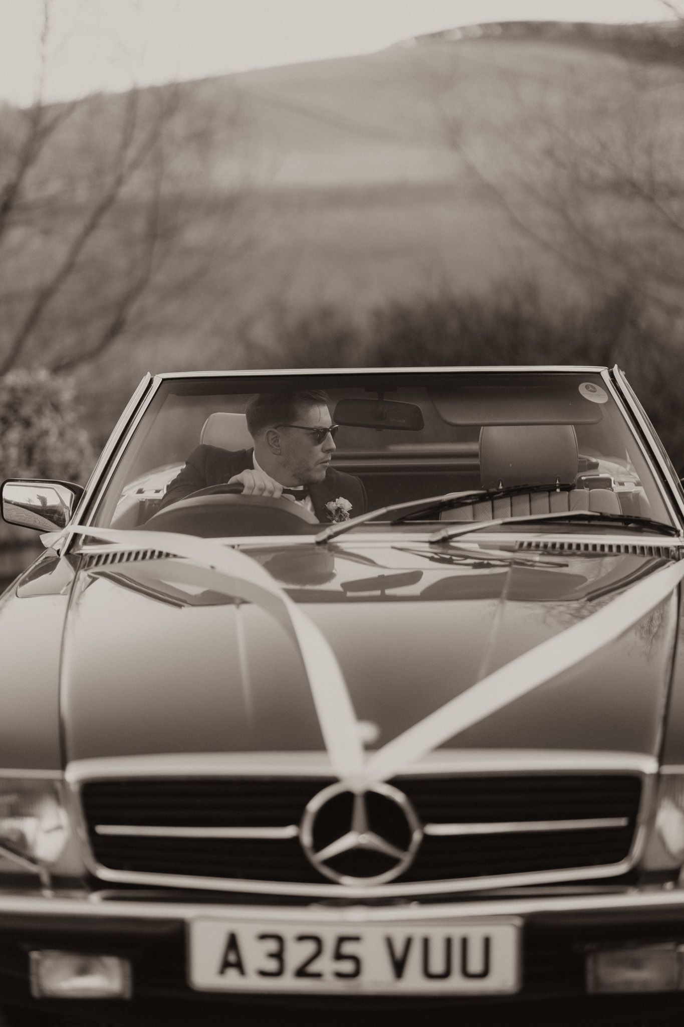 Classic black Mercedes-Benz convertible photographed in black and white with stylish driver behind the wheel.