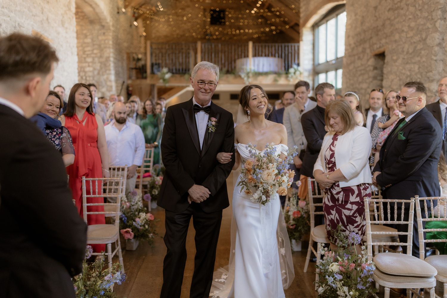Wedding ceremony in progress inside rustic stone barn venue with floral aisle decorations.