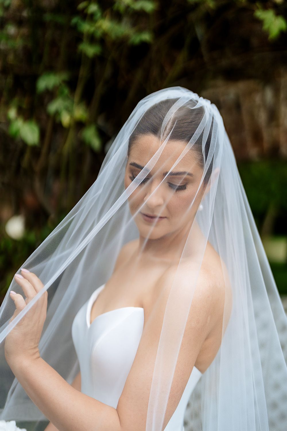 Beautiful bridal portrait with a delicate sheer veil against a soft green garden backdrop.