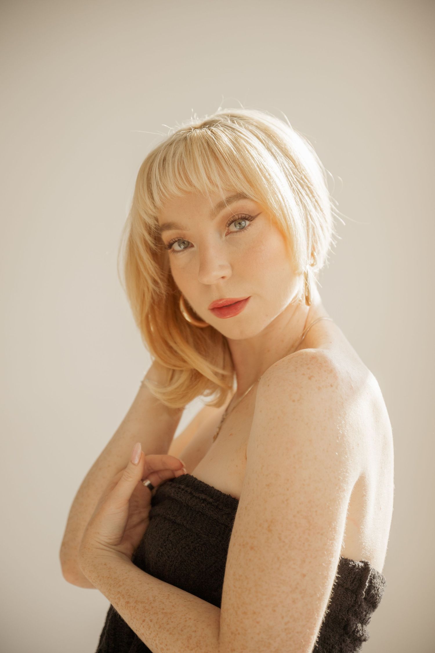 Portrait photograph showing blonde woman in black dress against beige backdrop with soft lighting.