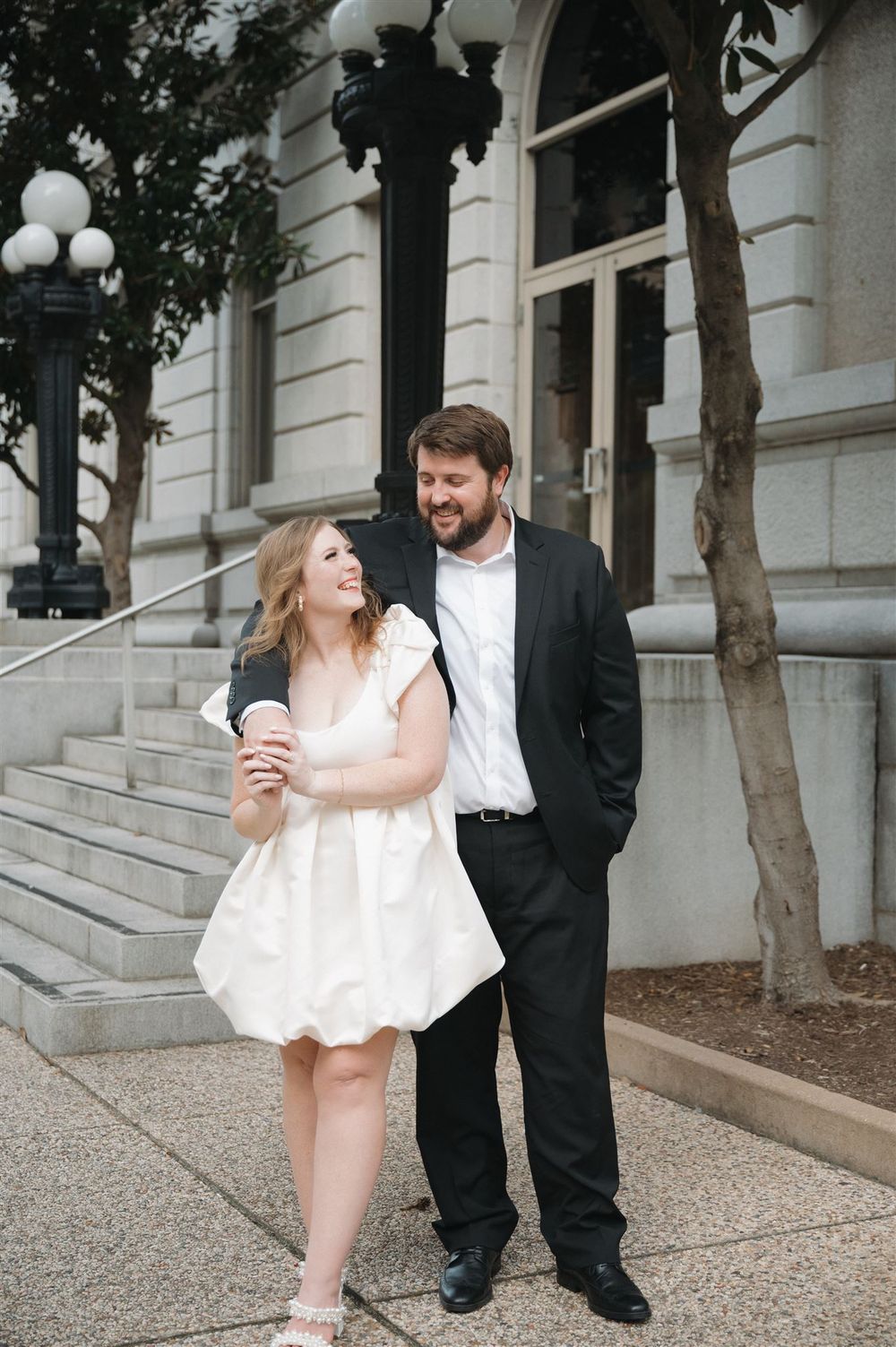 A couple shares a joyful moment on stone steps outside a historic building.