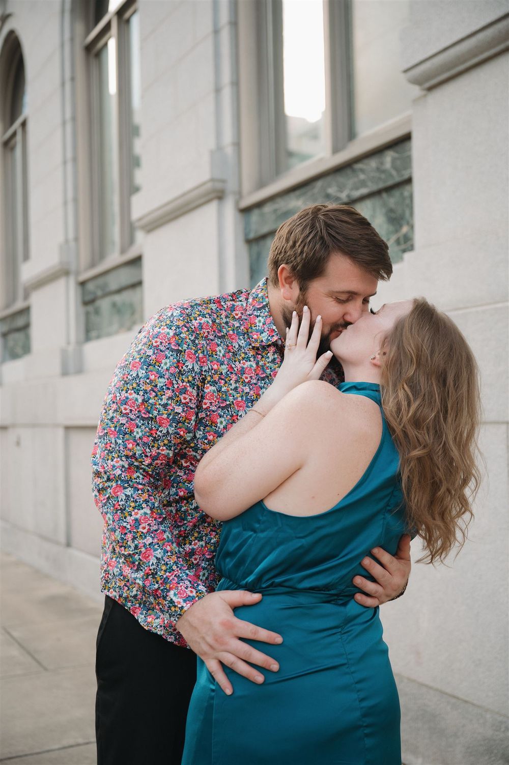 A romantic couple shares a passionate kiss against a stone building wall.