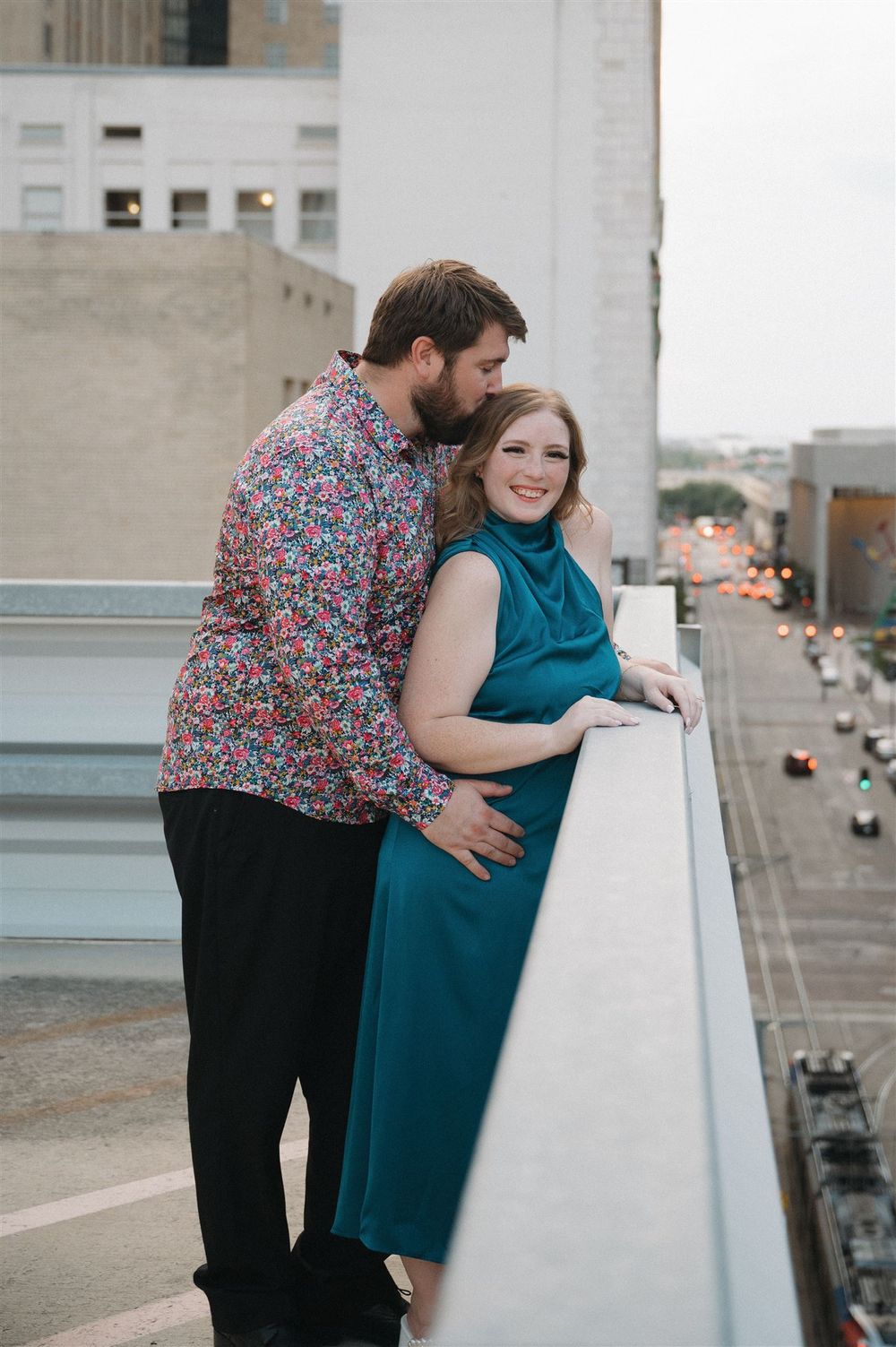 A couple sharing a romantic moment on an urban rooftop overlooking a city street with cars below.