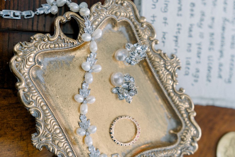 Wedding rings and delicate jewelry displayed on an ornate vintage gold tray with carved decorative borders.