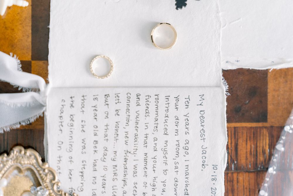 Wedding rings and handwritten vows on white paper with rustic wooden background.