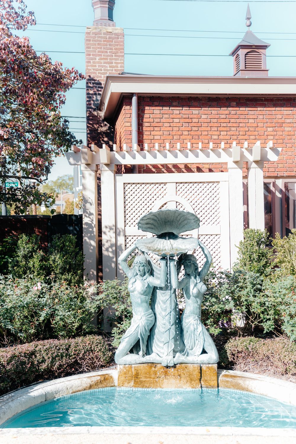 Decorative fountain with umbrella statues in a garden courtyard with brick building and pergola.
