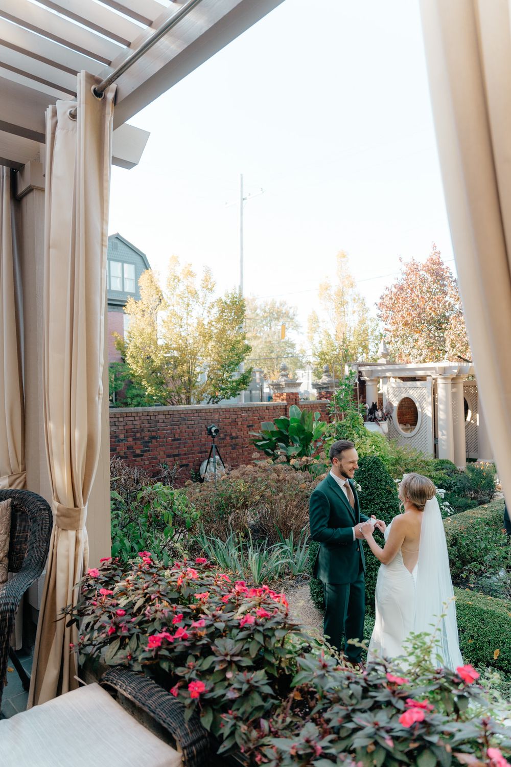 Wedding ceremony taking place on a covered patio with pink flowers and greenery in an elegant garden setting.