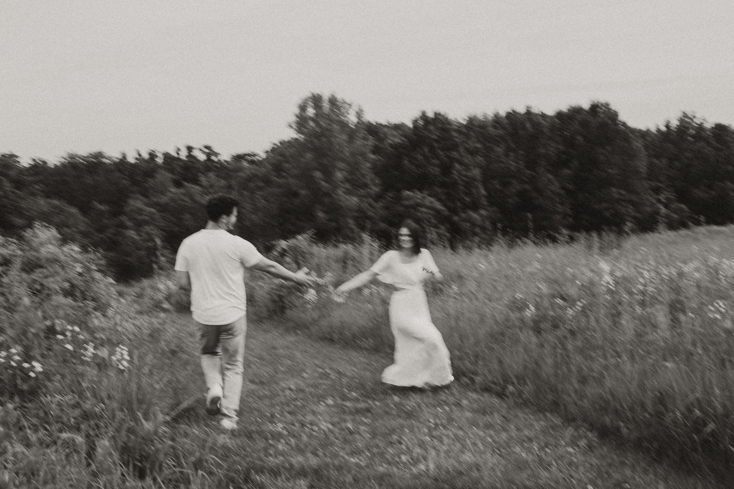 Couple dancing and laughing together in a sunny meadow with trees.
