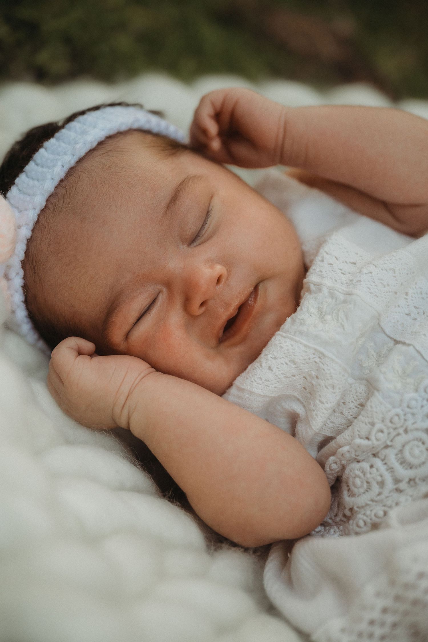 Peaceful sleeping infant in white lace outfit against soft knit background.