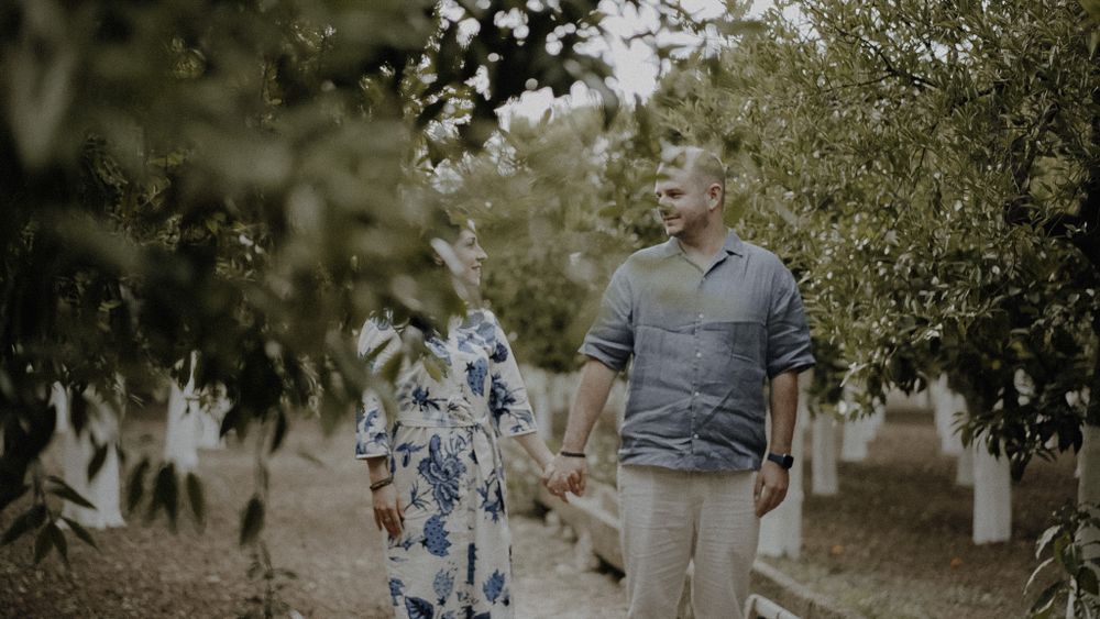 A couple walks through an orchard on a misty day.