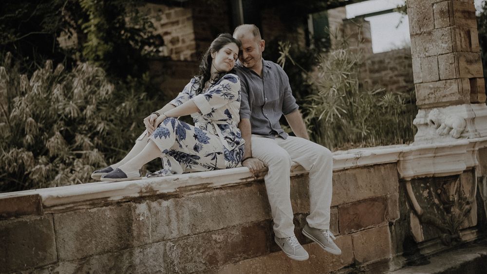 A couple sits together on a stone wall in a romantic outdoor setting.
