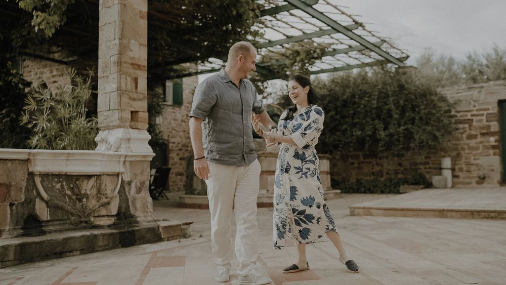 A couple dances together under a garden pergola in warm sunlight.