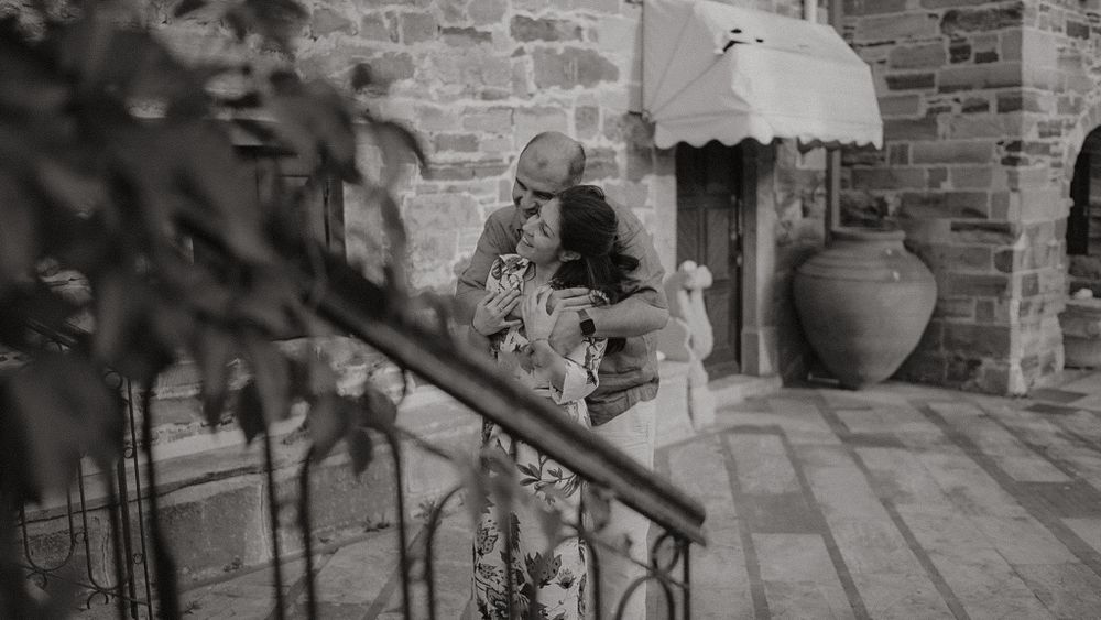 A person sits on stone steps next to a large decorative clay pot at a rustic building entrance.