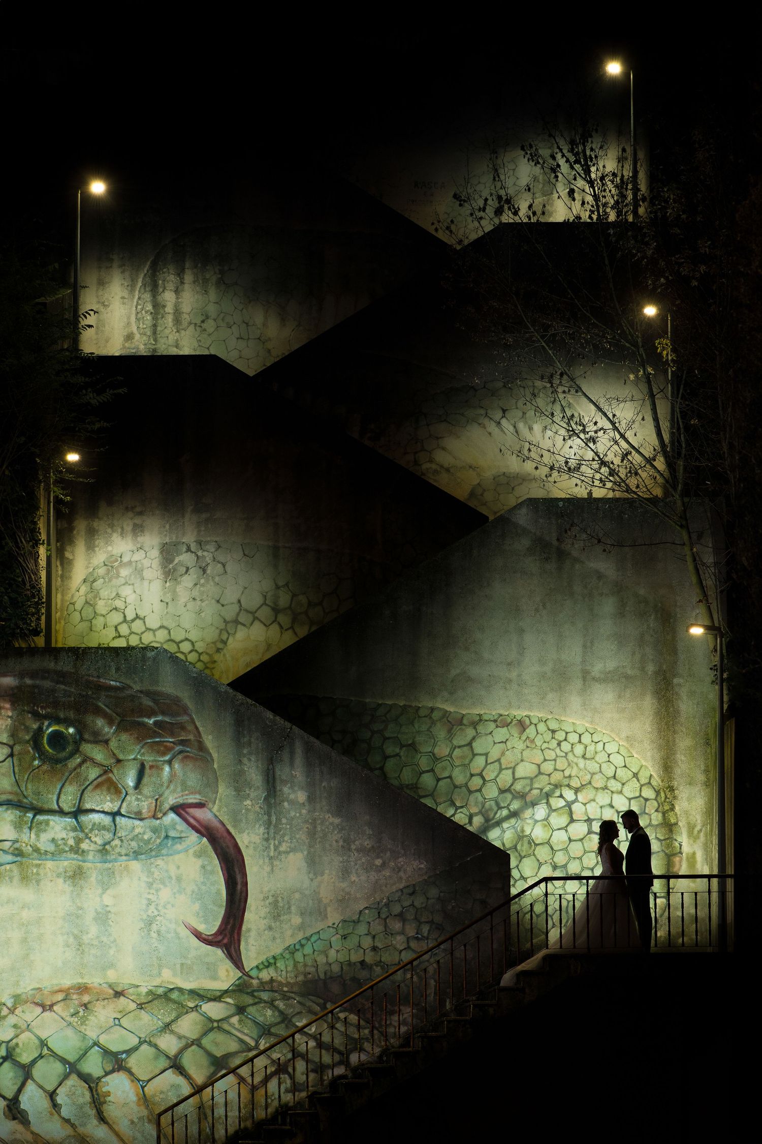 Silhouetted couple on stairs at night with illuminated street lamps and graffiti wall.