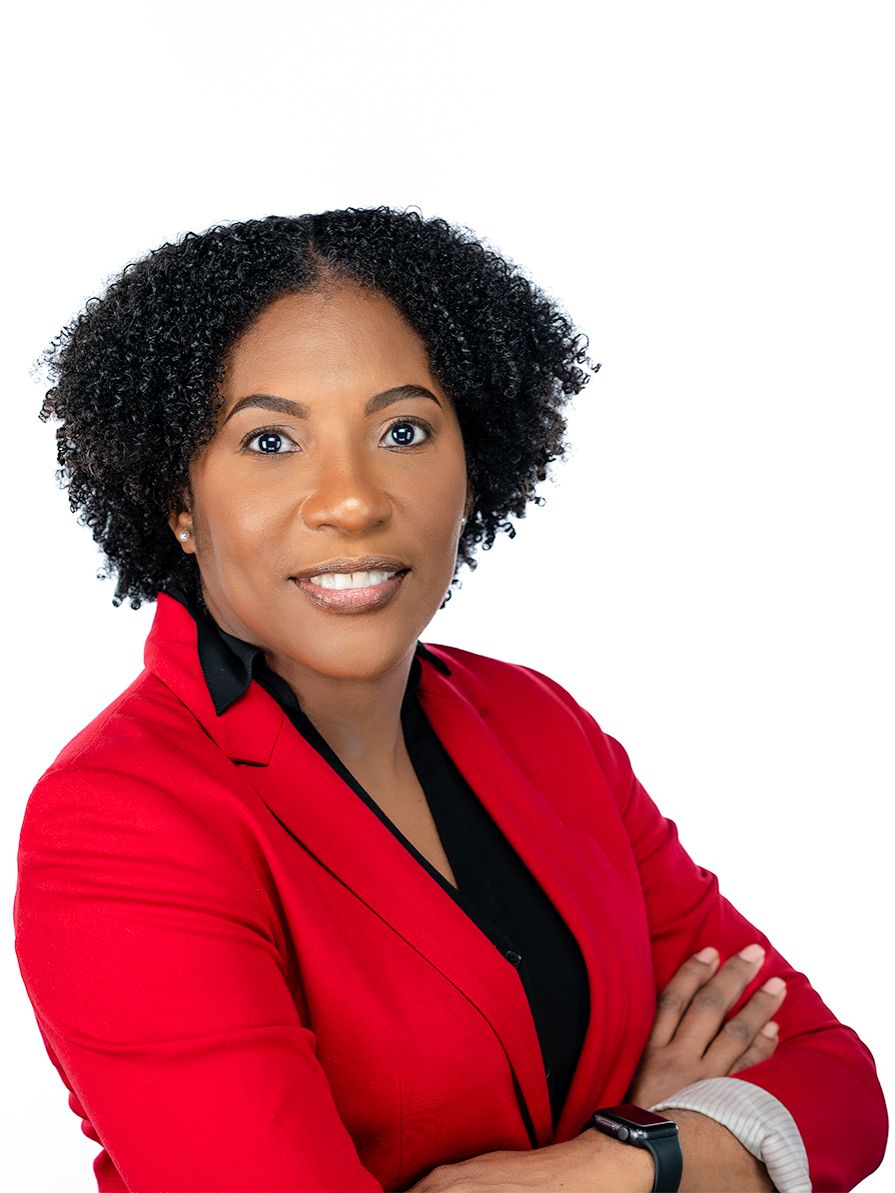 Professional portrait of a person in a bright red blazer and black top smiling confidently with arms crossed.