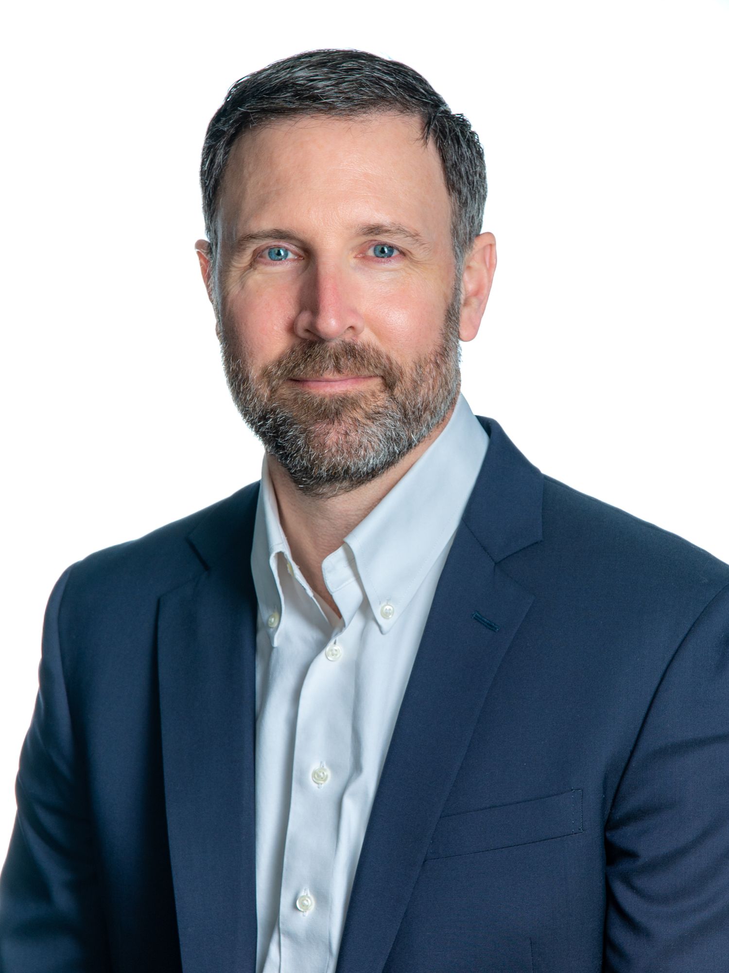Professional headshot photo of a person wearing a navy suit jacket and white button-down shirt against a white background.