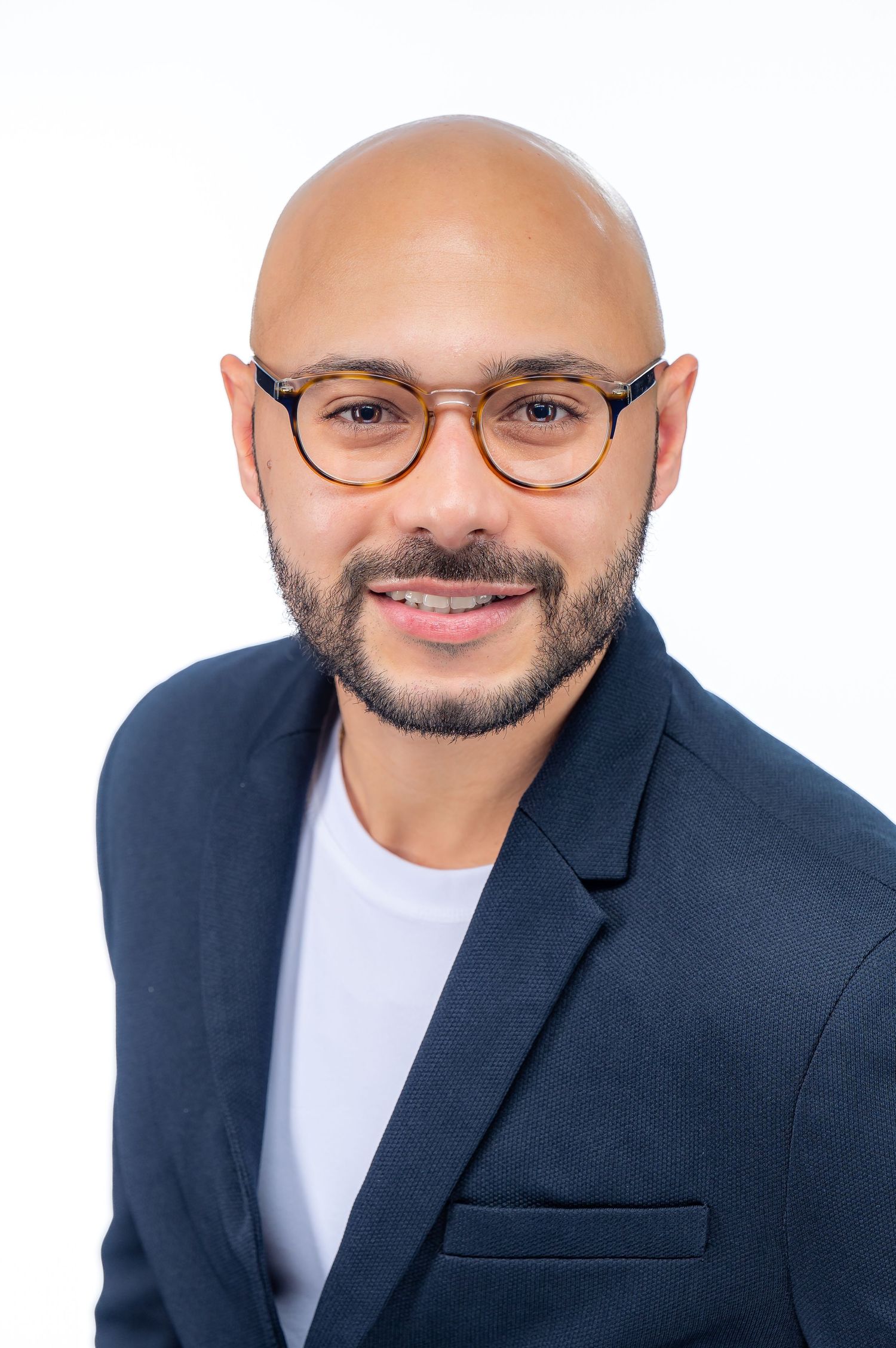 Professional portrait of a smiling person wearing glasses, a navy blazer and white t-shirt against a white background.
