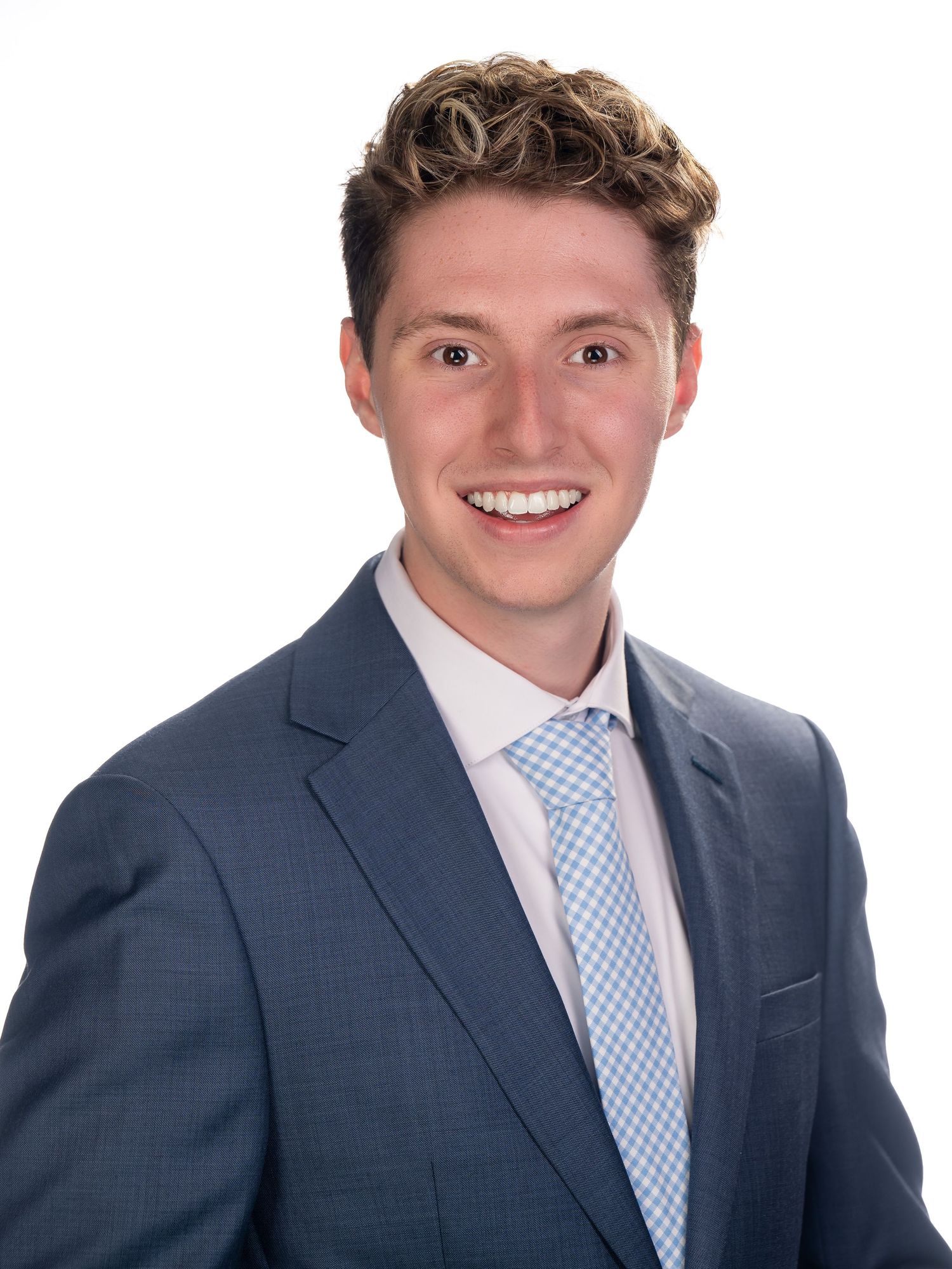 Professional headshot of a person in a navy suit and light blue checked tie smiling against white background.