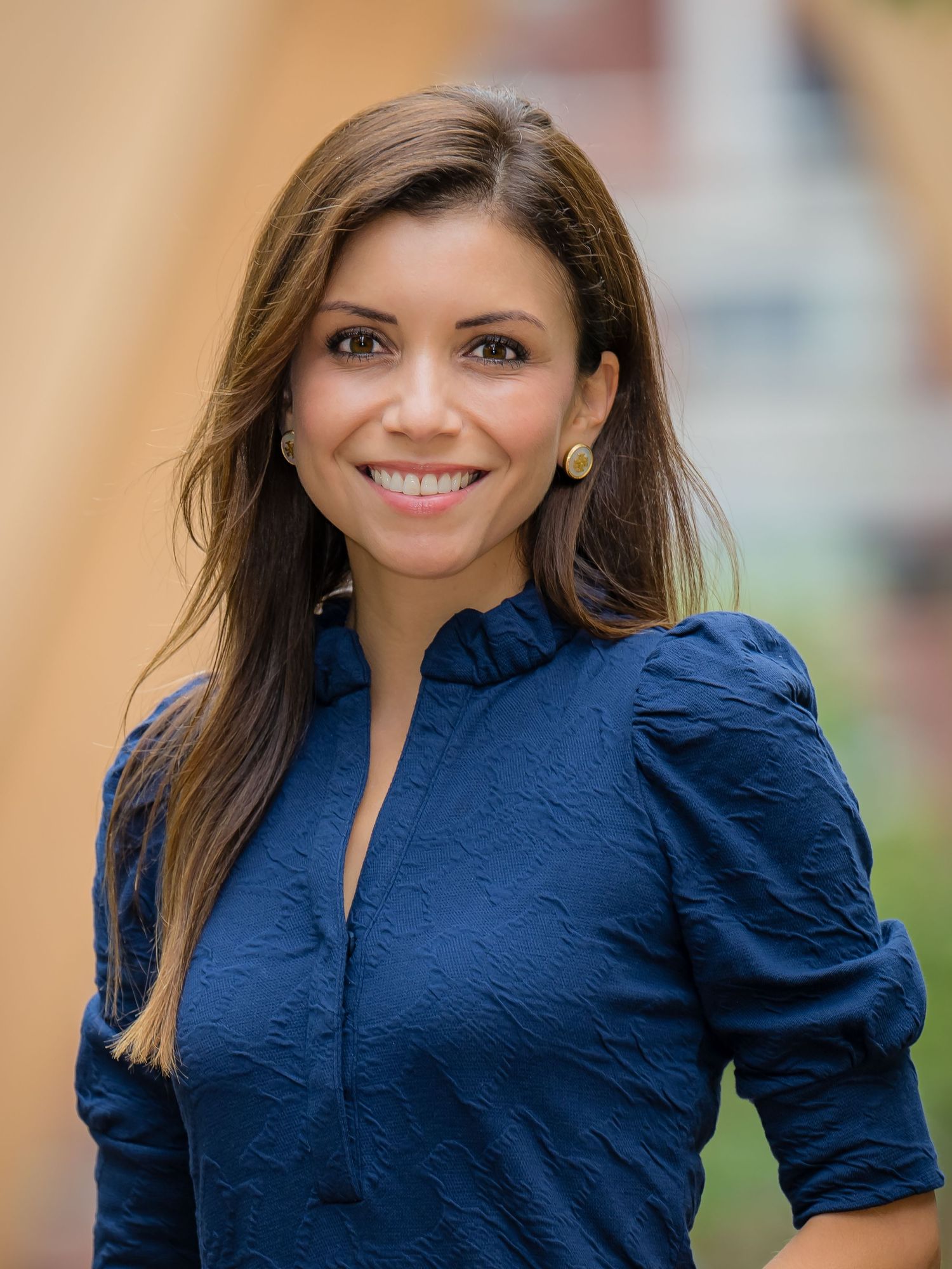 Professional headshot of person in navy blue blouse with puffed sleeves smiling warmly against blurred background.