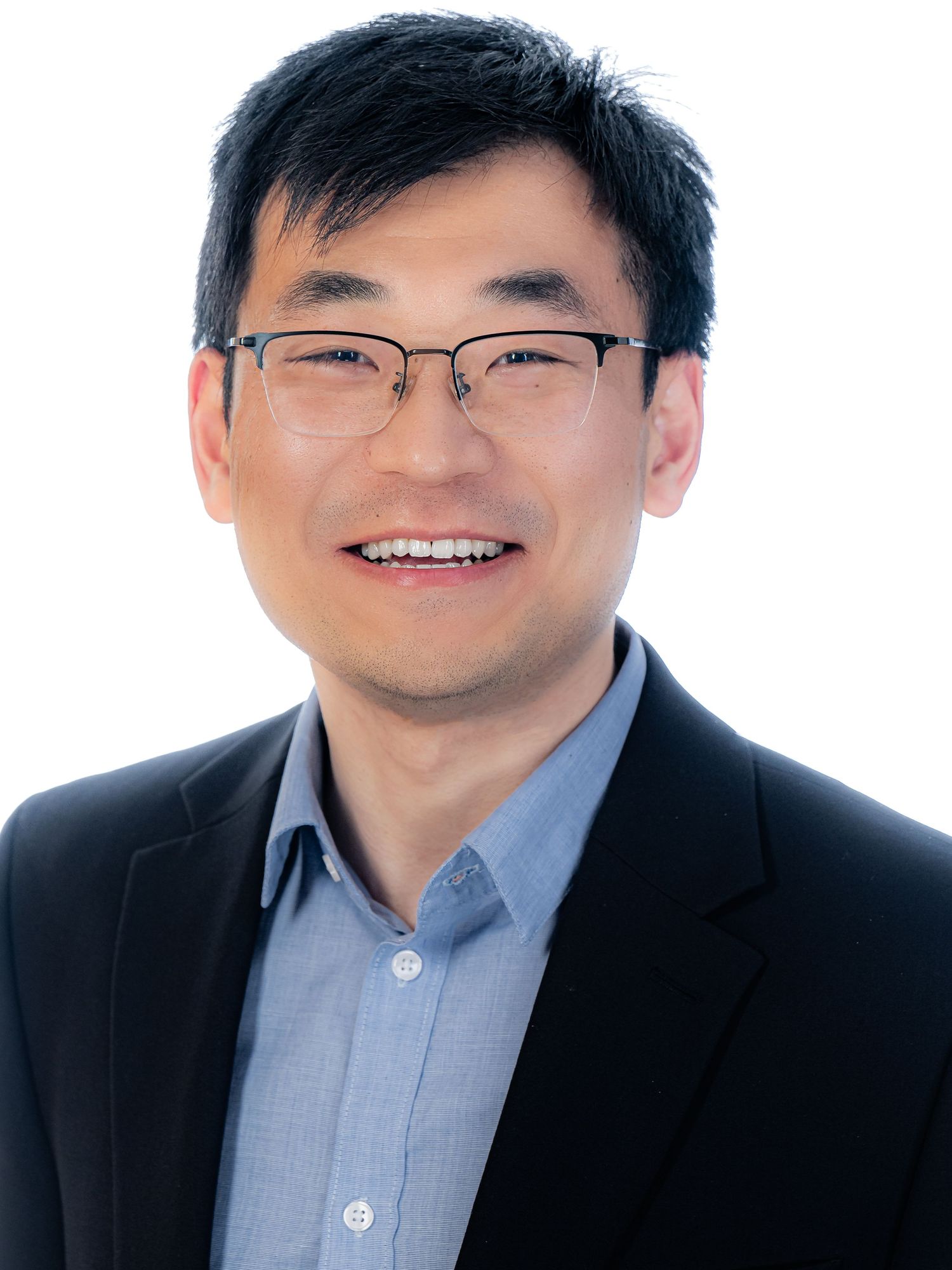 Professional headshot of someone in glasses wearing a dark blazer and blue button-up shirt against white background.