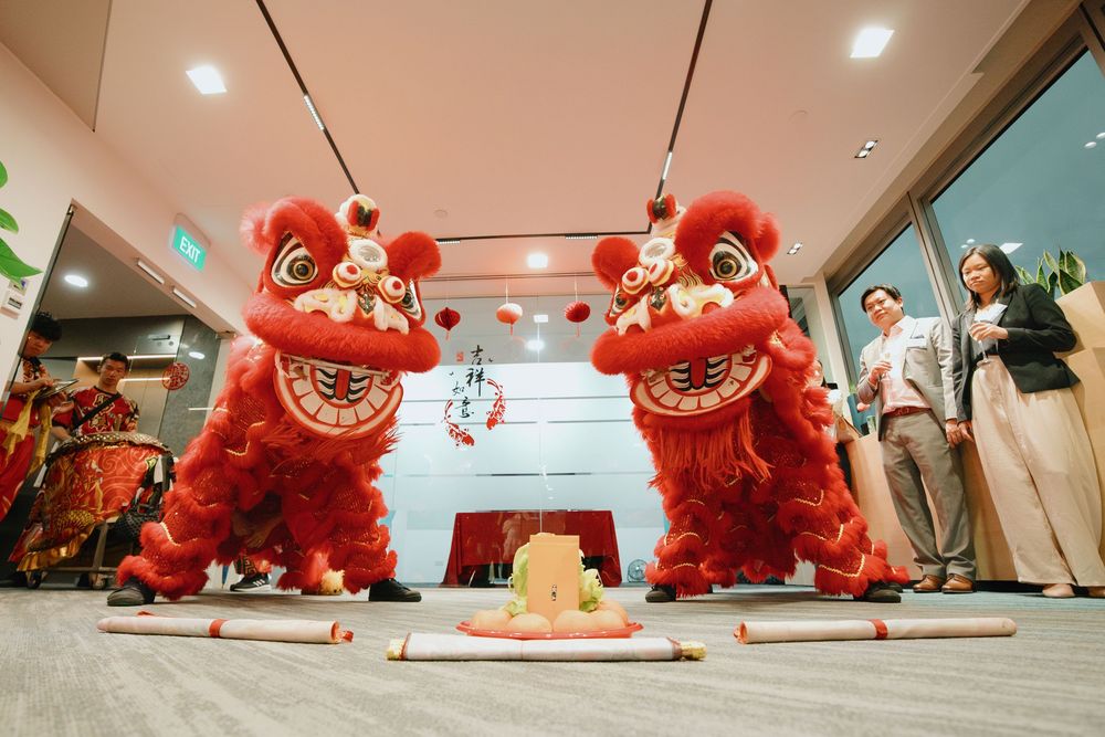 Two red Chinese lion dance costumes stand beside traditional decorations at an indoor celebration event.